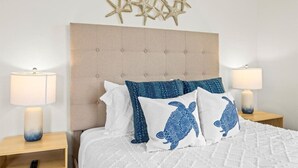 Un dormitorio con cabecera capitonada, dos lámparas de noche, cama con ropa de cama blanca y almohadas con estampado azul, y decoración de paredes con motivos de estrellas de mar.