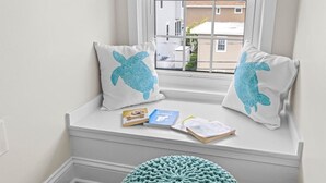 Asiento junto a la ventana con dos almohadones con diseño de tortuga marina, un reposapiés tejido y vistas a edificios.