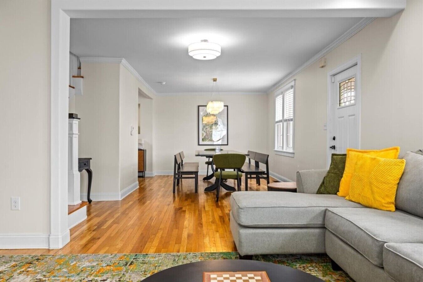 A living room with a gray sofa, wooden flooring, and a dining area with chairs and a table.