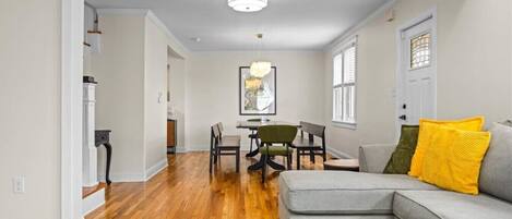 A living room with a gray sofa, wooden flooring, and a dining area with chairs and a table.