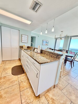 A kitchen with a granite countertop, white cabinets, a large island, and a view of the ocean. - Beachfront, Gulf Views from Every Room + Dogs Welcome (Panama City Beach)