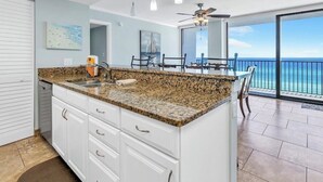 A kitchen with a granite countertop, white cabinets, and a view of the ocean. - Beachfront Panama City Beach Condo with Unobstructed Gulf Views (Panama City Beach)