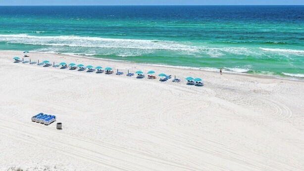 A beach with a row of umbrellas and lounge chairs, a clear sky, and the ocean in the background. - Beachfront Panama City Beach Condo with Unobstructed Gulf Views (Panama City Beach)