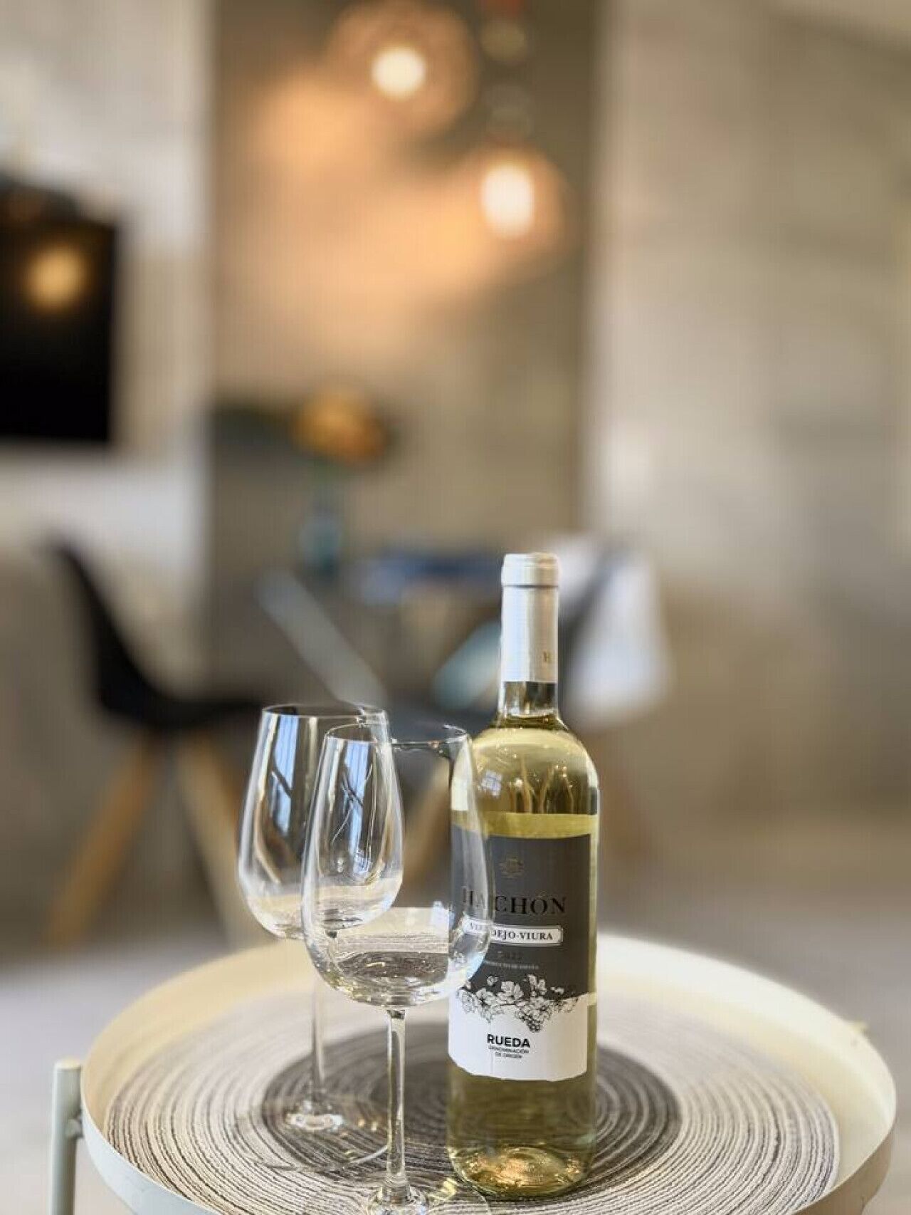 Een fles wijn en twee glazen op een ronde tafel met een structuur.
