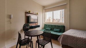 Una habitación con televisor, sofá, cama, mesa con sillas y ventana con vista a la ciudad.