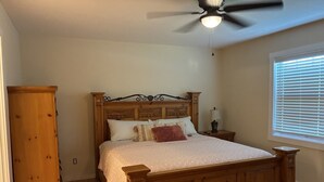 Ein Schlafzimmer mit einem hölzernen Bett, einem Nachttisch, einer Lampe, einem Deckenventilator und einem Fenster mit Jalousien.