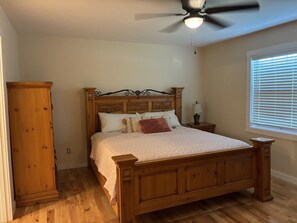 Ein Schlafzimmer mit einem hölzernen Bett, einem Nachttisch, einer Lampe, einem Deckenventilator und einem Fenster mit Jalousien.