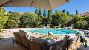 Un área junto a la piscina con una silla de descanso, un sofá y una mesa lista para comer.
