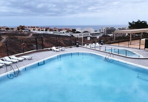 Ein Swimmingpool mit Liegestühlen, einem Rettungsring und Blick auf Gebäude sowie das Meer.