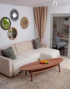 Ein Wohnzimmer mit einer Couch, einem Couchtisch mit Obst und Blick auf einen Balkon.