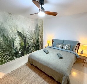 Ein Schlafzimmer mit Bett, Deckenventilator, Wandgemälde und zwei Nachttischlampen.