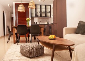 Ein modernes Wohnzimmer mit Couch, Esstisch und Stühlen sowie einer Küche im Hintergrund und einem Holztisch.
