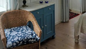 Una habitación con una silla de mimbre, un armario azul, un espejo y un cuadro en la pared.