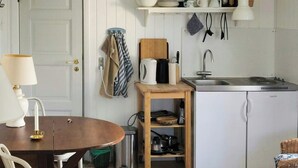 Cocina compacta con lavamanos, estufa y armarios blancos. Cuenta con una mesa de comedor, sillas y una lámpara.