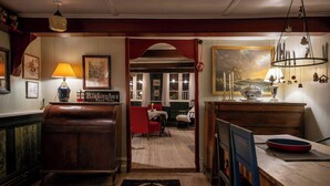 A wooden interior with a red chair, a table with a red plate, and a hanging light fixture. - Historic stay in the heart of Aeroskobing (Ærøskøbing)