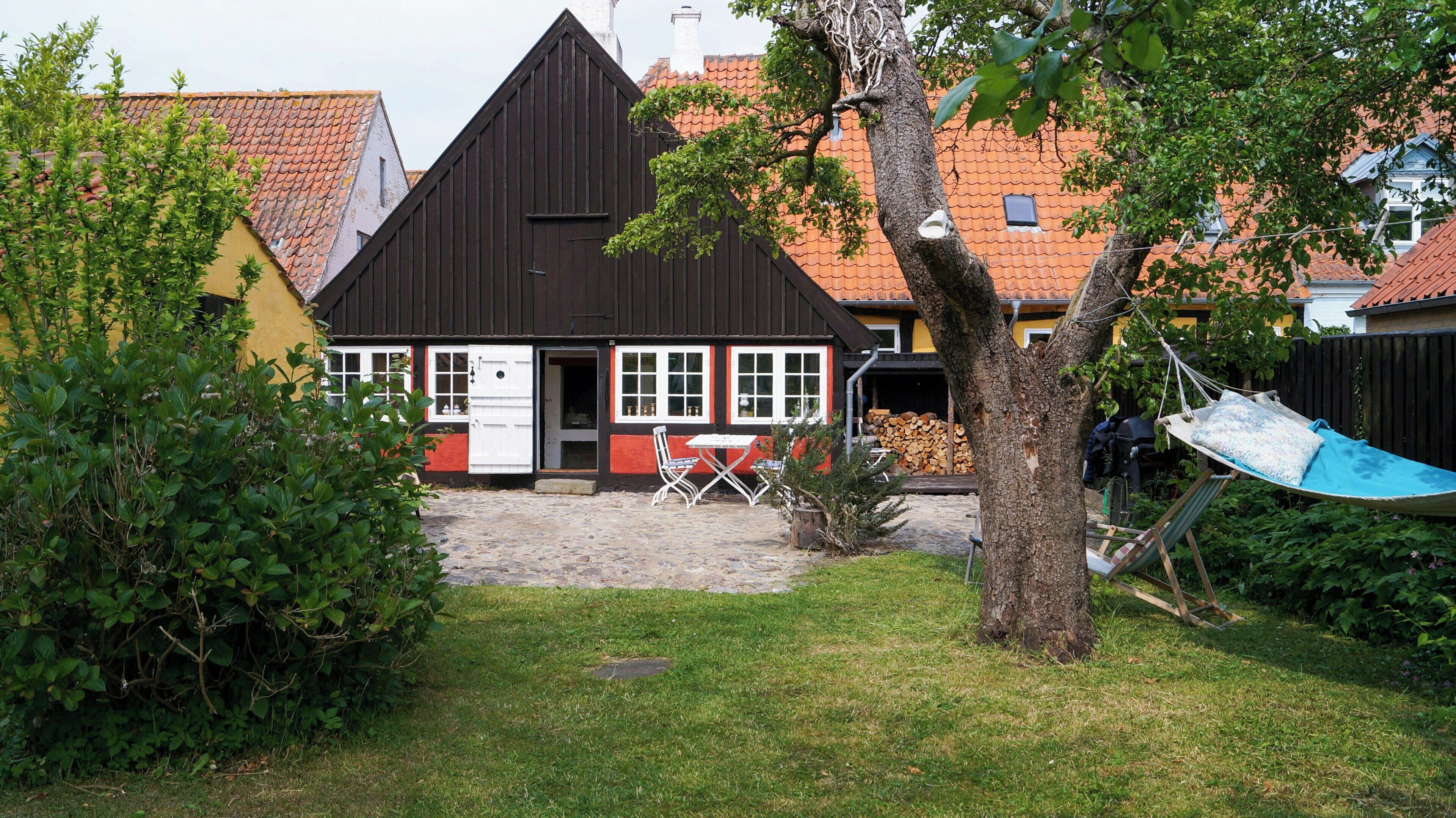 A house with a black roof, white windows, and a small garden with a hammock.