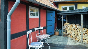 A red and black building with a blue door, a white chair with a striped cushion, and a stack of firewood.