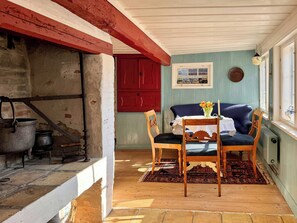 A room with a fireplace, a table with chairs, a red door, and a window with a view.