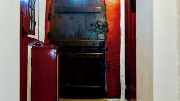 A narrow hallway with a wooden door at the end, a red wall, and a stone floor.