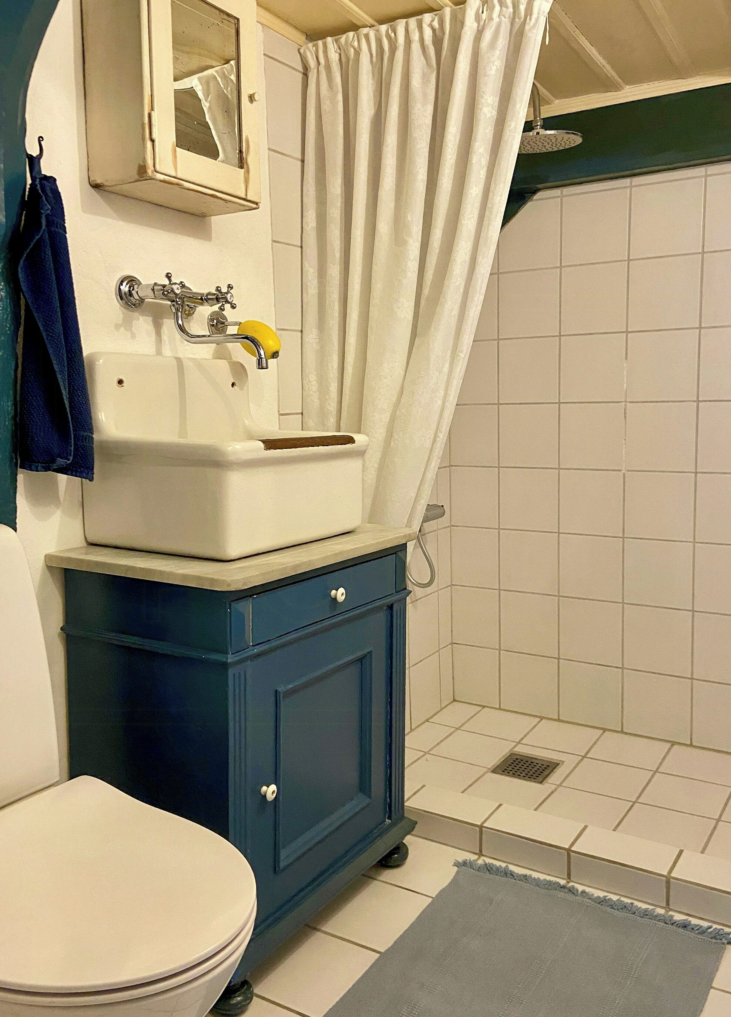 Un baño con inodoro, lavamanos con espejo, cortina de ducha y un armario azul.