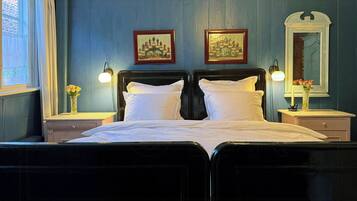 A double bed with white linens, two bedside tables with lamps, a mirror, and two framed pictures on the wall.