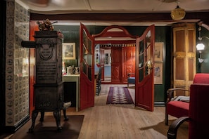 A room with a wooden floor, a red chair, a wooden cabinet, and a door leading to another room.