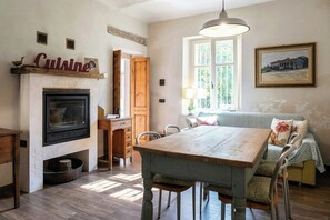 A dining area with a wooden table and chairs, a fireplace, and a window with a view of greenery. - Grandmother's house with hot tub in Scurzolengo (Scurzolengo)