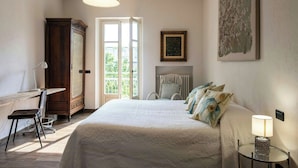 Un dormitorio con cama, escritorio, silla, armario, radiador, lámpara y ventana.