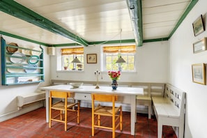 A kitchen with a white table, two wooden chairs, a bench, and a window with curtains.