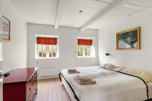 A bedroom with a bed, two windows with red valances, a red dresser, and a framed picture on the wall.