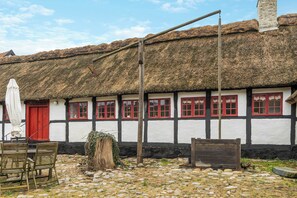 A traditional building with a thatched roof, white walls with black timber framing, red windows, and a stone-paved courtyard.