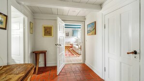 Um corredor com uma mesa de madeira, uma porta e vista para um quarto com um tapete estampado.