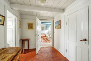 A hallway with a wooden table, a door, and a view into a room with a patterned rug. - Timber-framed farm on Reersø with cobblestone yard (Gørlev)