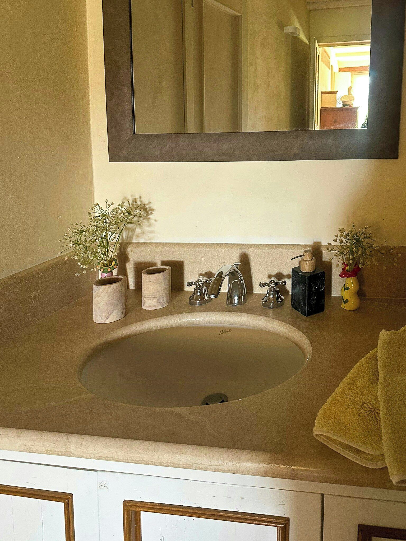 A bathroom with a beige sink, two faucets, a mirror, and a towel on the counter.