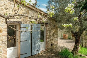 A stone building with two white doors, a tree with blossoms, and a stone wall. - Historical panoramic villa with pool, Umbria (Perugia)