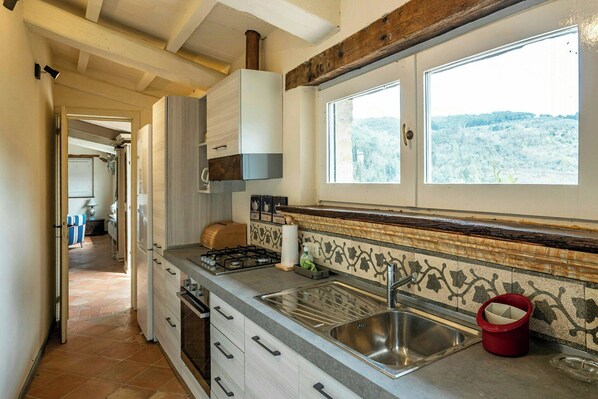 A kitchen with a stove, sink, and window overlooking a snowy landscape. - Historical panoramic villa with pool, Umbria (Perugia)