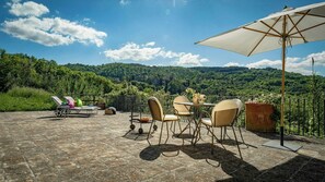 A terrace with outdoor furniture, a table, and an umbrella, overlooking a lush green landscape. - Historical panoramic villa with pool, Umbria (Perugia)