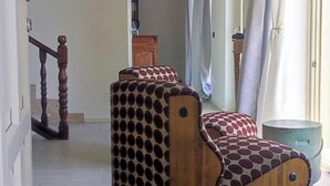 Een kamer met een houten bank met ronde uitsparingen, een betegelde vloer, een trap en een raam met gordijnen.