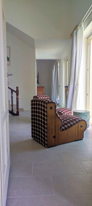 Une pièce avec un banc en bois doté d’ouvertures circulaires, un sol carrelé, un escalier et une fenêtre avec des rideaux.