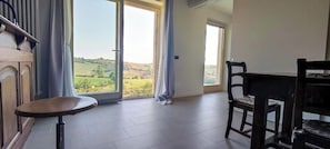 Une pièce dotée d’une grande fenêtre, d’une chaise en bois, d’une petite table ronde et offrant une vue sur un paysage verdoyant.