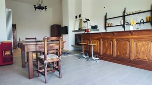 Een eetgedeelte met een houten tafel en stoelen, een rode kast, een televisie en een keukenblad met een spoelbak en planken.