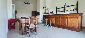 Un coin repas avec une table et des chaises en bois, un buffet rouge, un téléviseur et un plan de travail de cuisine avec un évier et des étagères.
