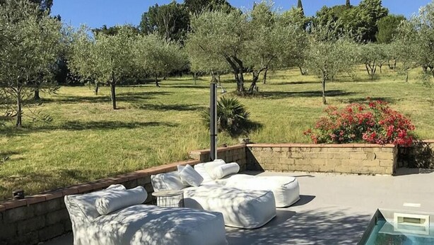 Zona junto a la piscina con mobiliario exterior y vistas a un jardín ajardinado.
