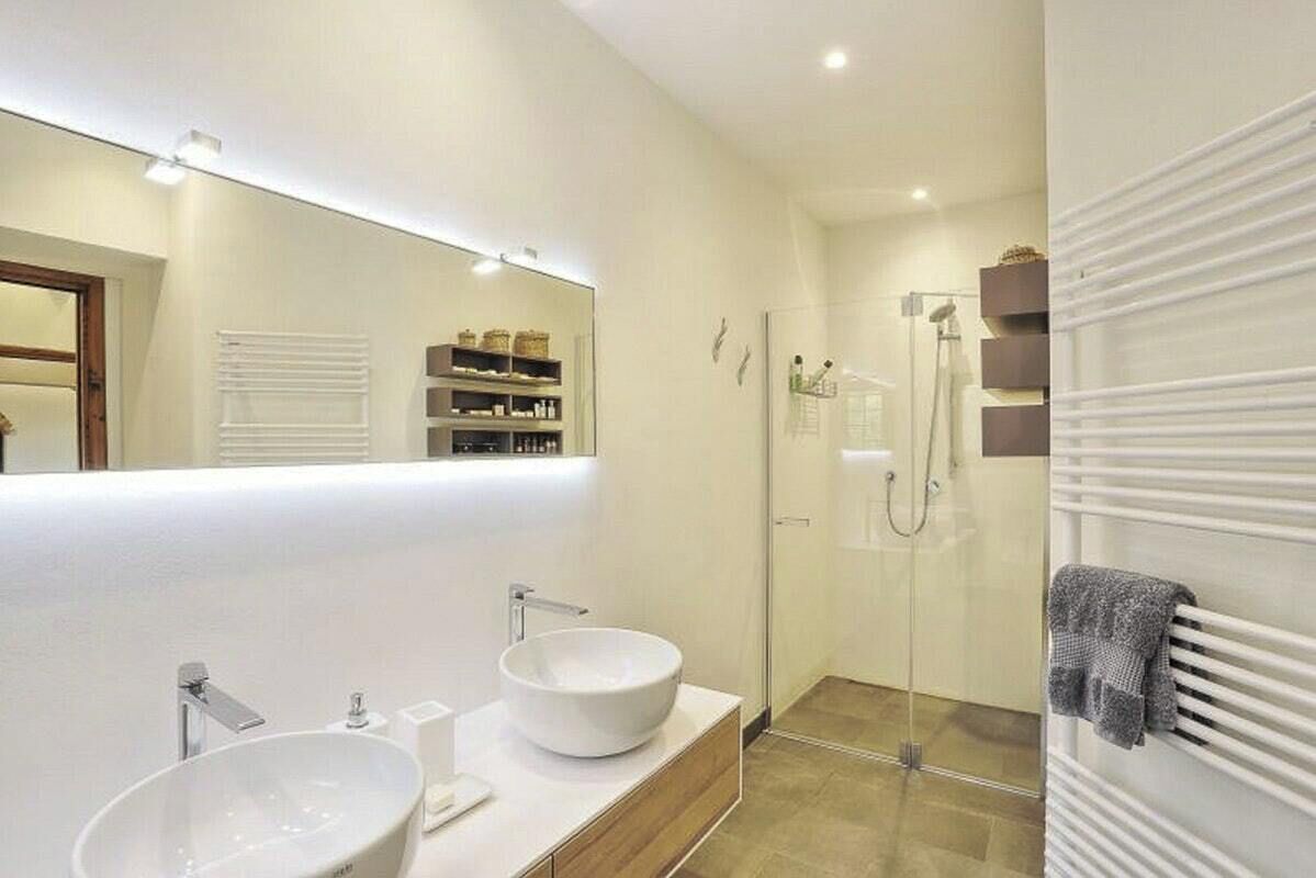 Une salle de bain moderne avec un grand miroir, deux lavabos, une douche et un porte-serviettes.