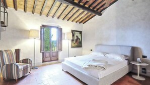 Un dormitorio con una cama grande, una silla, una lámpara y un cuadro en la pared.
