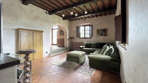Un salón con un sofá verde, un mueble de madera, un tapiz estampado y un techo con vigas a la vista.