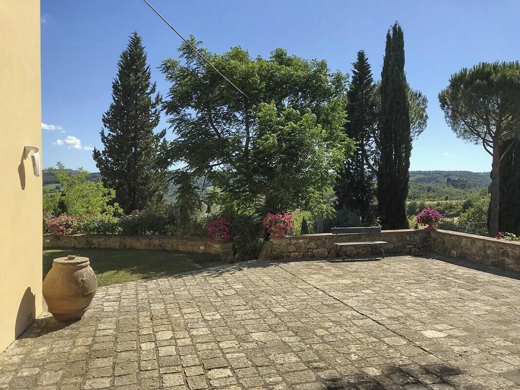Une cour dallée de pierres, un grand vase et une variété d’arbres et d’arbustes.
