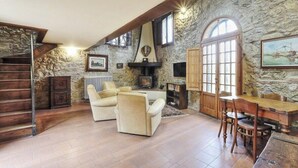 Una habitación con paredes de piedra, una chimenea, una escalera de madera y un comedor con sillas y una mesa.