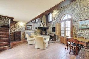 A stone-walled room with a fireplace, a wooden staircase, and a dining area with chairs and a table. - Tuscan estate with pool in the heart of Chianti (Impruneta)