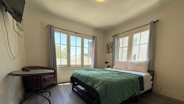A bedroom with a bed, a small table, and two windows. - Comfortable Studio Unit on 2nd Floor (Los Angeles)